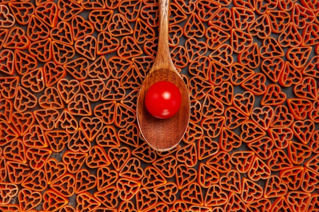 Foto grátis vista superior do tomate cereja na colher na massa italiana de corações vermelhos na mesa escura