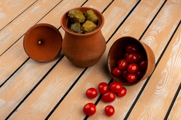 Foto grátis vista superior dolma, juntamente com tomates-cereja vermelhos dentro de panelas marrons na mesa de madeira