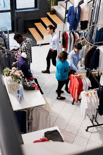Foto grátis vista superior dos clientes que compram roupas formais em boutiques modernas, comprando roupas elegantes da nova coleção de moda. diversas pessoas olhando para cabides cheios de mercadorias da moda na loja