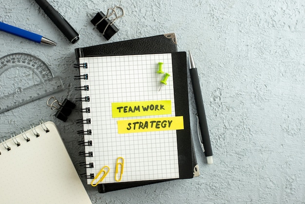 Vista superior dos escritos de estratégia de trabalho em equipe em folhas coloridas no caderno espiral e na régua do livro no fundo de areia cinza