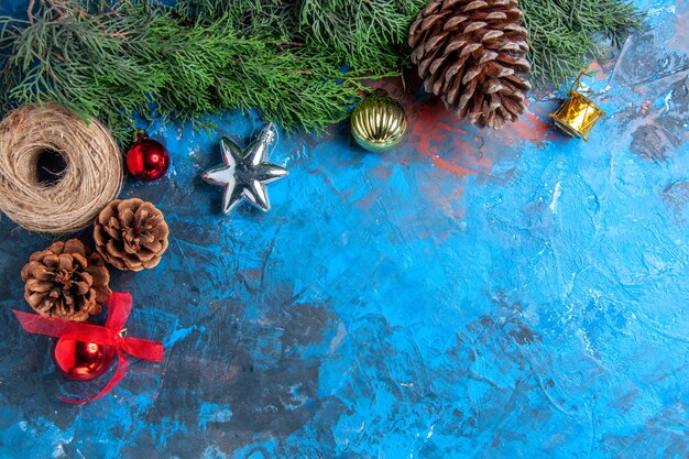 Vista superior dos galhos de pinheiro com fio de palha de pinhas brinquedos de Natal na superfície azul-vermelha