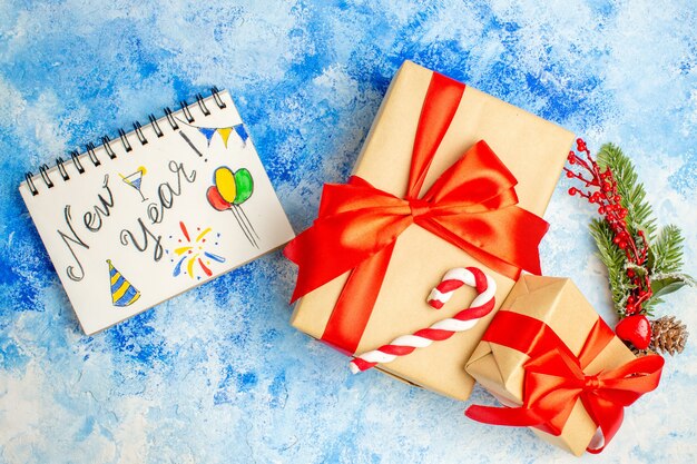 Vista superior dos presentes de Natal amarrados com laço vermelho de ano novo escrito no bloco de notas na mesa azul