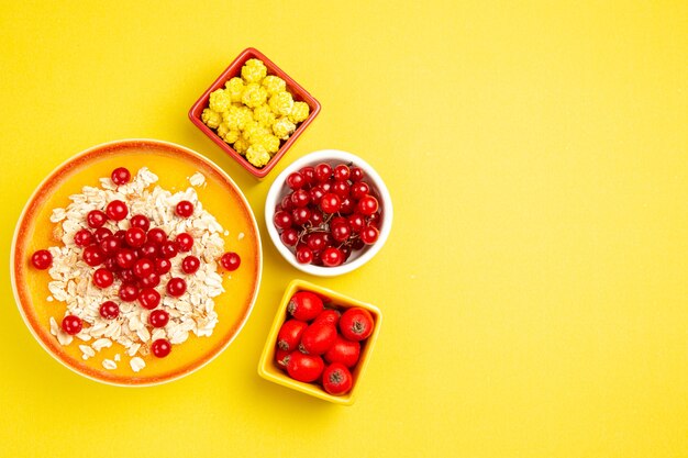 Vista superior em close-up com frutas diferentes, frutas vermelhas, doces e aveia, aveia na mesa amarela
