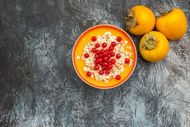 Vista superior em close-up com frutas vermelhas na tigela ao lado dos três apetitosos caquis