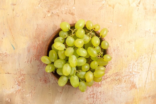 Foto grátis vista superior em close-up da tigela de uvas com cachos de uvas verdes na mesa de creme