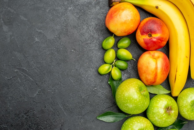 Vista superior em close-up das frutas na mesa, maçãs verdes com folhas, bananas e nectarinas amarelas