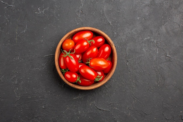 Vista superior em close-up de tomates em uma tigela tomates vermelhos maduros em uma tigela no centro da mesa escura