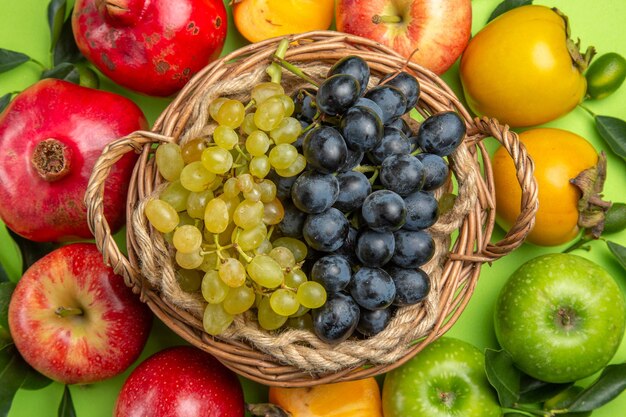 Vista superior em close-up frutas coloridas romã maçãs caquis folhas cesta de uvas