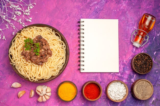Vista superior espaguete cozido com carne moída em prato de massa de macarrão de mesa rosa