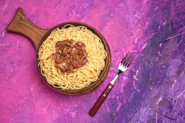 Vista superior espaguete cozido com carne moída em tempero de massa de massa de mesa rosa