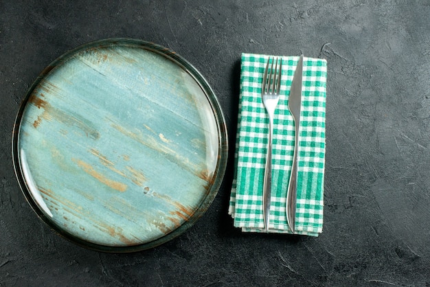 Vista superior faca e garfo de prato redondo em guardanapo xadrez verde e branco em mesa preta