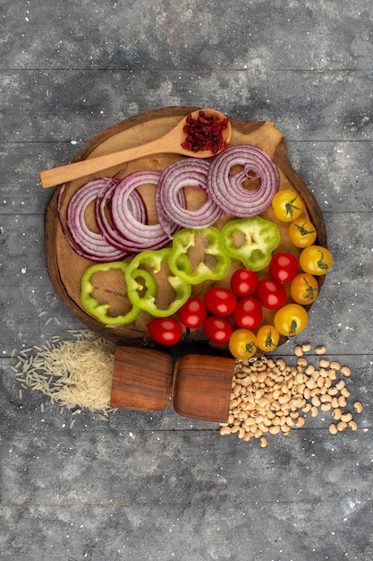 Foto grátis vista superior fatiada de legumes, como cebola e pimentão verde, juntamente com tomates vermelhos inteiros e tomates amarelos no chão cinza