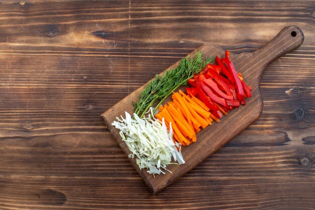 Vista superior fatiada de legumes, repolho, cenoura, verduras e pimenta na superfície da tábua de cortar marrom