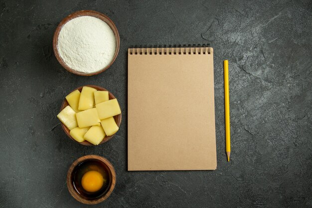 Vista superior fatiada de queijo com farinha e bloco de notas em fundo cinza farinha de massa alimentos crus cozer