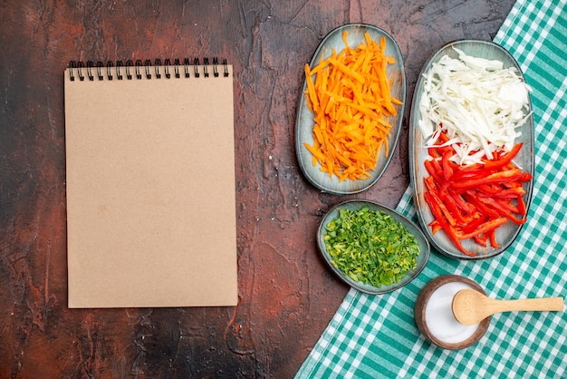 Vista superior fatiada de vegetais, cenoura, repolho e pimentão com verduras na mesa escura