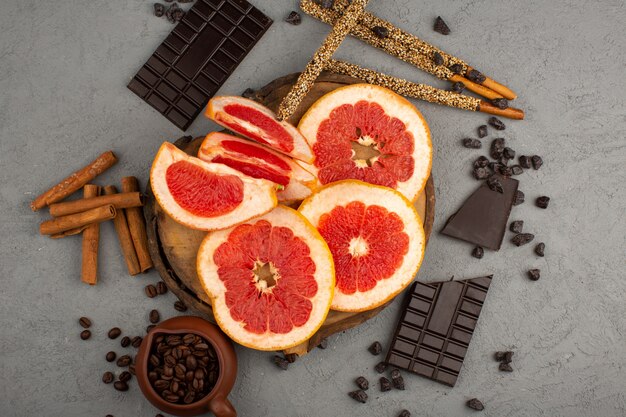 vista superior fatiadas de toranjas maduras, juntamente com barras de chocolate e canela no fundo cinza