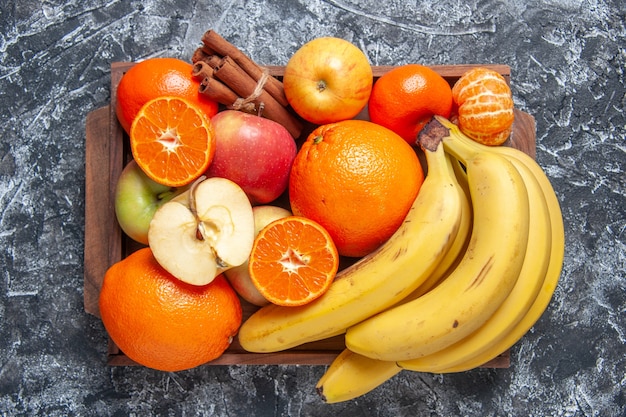 Vista superior frutas frescas bananas maçãs laranjas canela em pau na bandeja de madeira na mesa