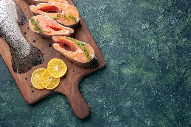 Foto grátis vista superior horizontal de fatias de limão de peixes crus frescos, verdes, pimenta na tábua de madeira na mesa de cores escuras