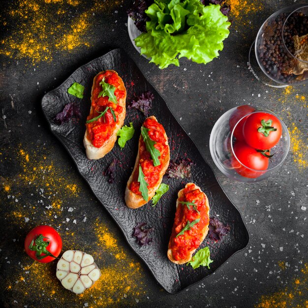 Vista superior lanche com e fatias de pão acima de salada de tomate e rúcula em placa escura