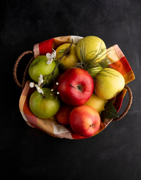 Vista superior maçãs coloridas em uma cesta com um raminho de flores