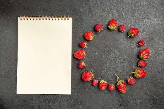 Vista superior, morangos frescos e vermelhos, alinhados com frutas silvestres de cor cinza-escuro