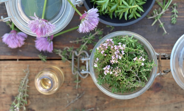 Vista superior no frasco de vidro cheio de ervas aromáticas e frasco de óleo na mesa de madeira