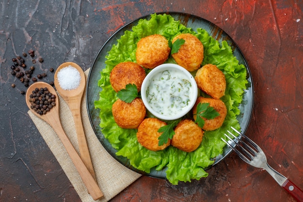 Vista superior nuggets de frango, garfo de alface no prato sal e pimenta-do-reino em colheres de madeira na mesa escura