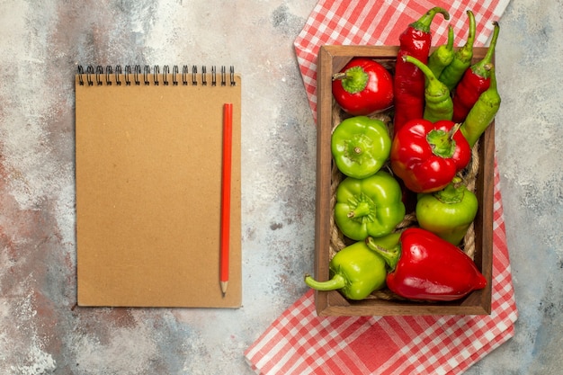 Vista superior pimentas vermelhas e verdes pimentas quentes em caixa de madeira no caderno de toalha de mesa quadriculada lápis vermelho na superfície nua