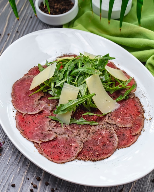 Vista superior prato de carne basturma com rúcula e queijo parmesão