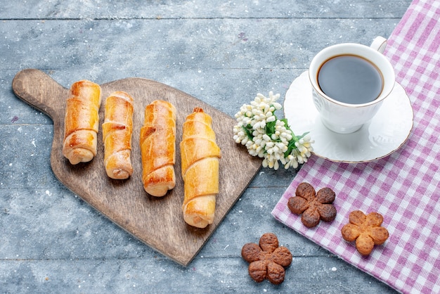 Vista superior, pulseiras deliciosas e doces com recheio, juntamente com uma xícara de biscoitos de café na mesa de madeira cinza.