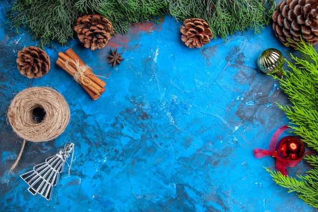 Vista superior ramos de pinheiro fio de palha paus de canela brinquedos de árvore de natal em fundo azul-vermelho