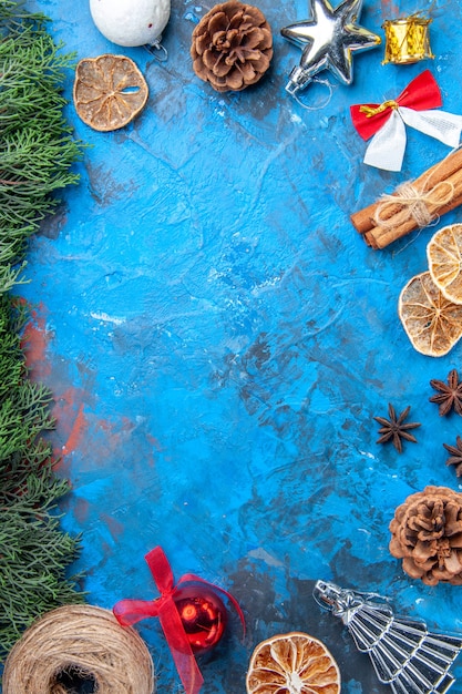 Vista superior ramos de pinheiro fio de palha varas de canela secas fatias de limão sementes de anis brinquedos coloridos para árvores de natal na superfície azul-vermelha