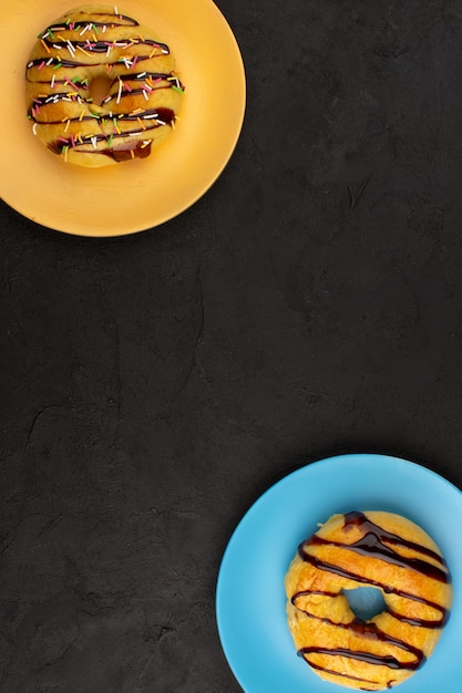 Foto grátis vista superior rosquinhas doce gostoso delicioso dentro de placas coloridas sobre o fundo escuro