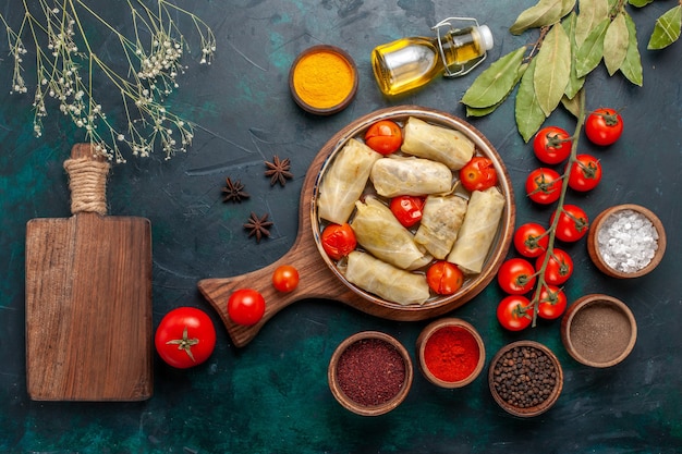 Vista superior saborosa refeição de carne enrolada dentro de repolho com óleo de temperos e tomates frescos na mesa azul escura