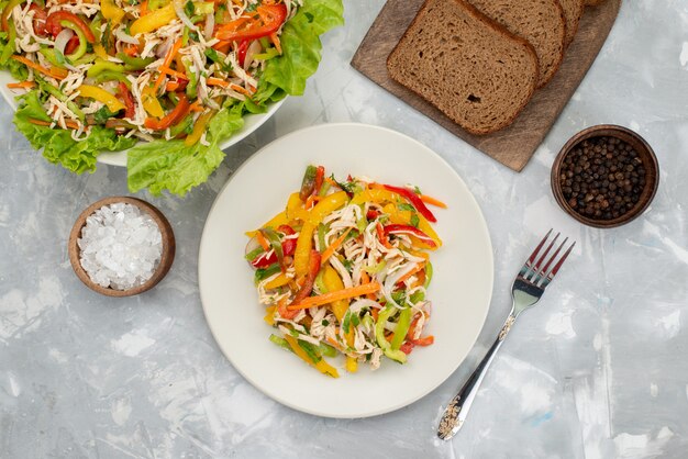 Vista superior saborosa salada de legumes com legumes fatiados e salada verde com pão em cinza, refeição salada de legumes