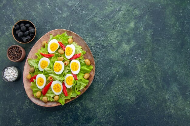 Vista superior saborosa salada de ovo com salada verde de azeitonas e temperos em fundo azul escuro