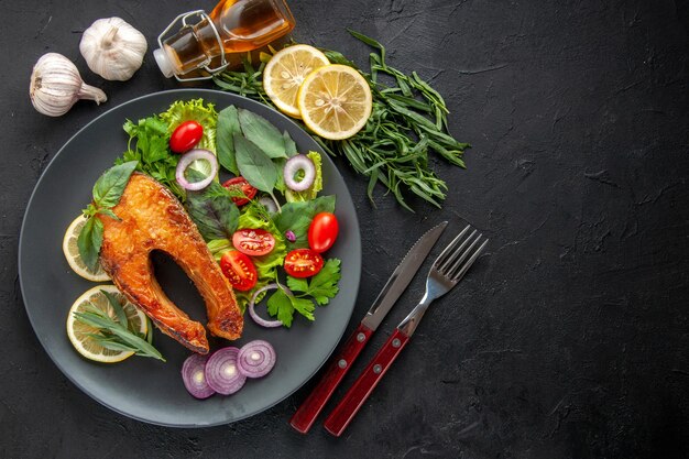 Vista superior saboroso peixe cozido com legumes frescos e temperos no prato de carne de comida de cor de mesa escura foto