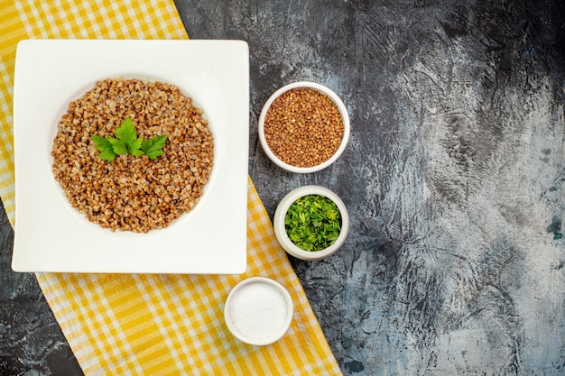 Vista superior saboroso trigo sarraceno cozido em prato branco com verduras em mesa cinza claro