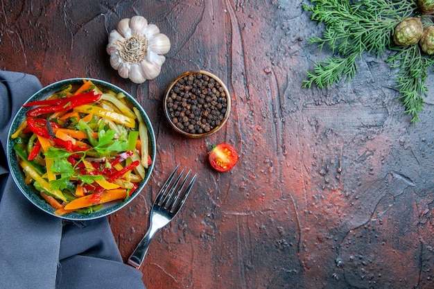 Vista superior salada de legumes em uma tigela xale azul ultramar garfo de alho pimenta preta em mesa vermelha