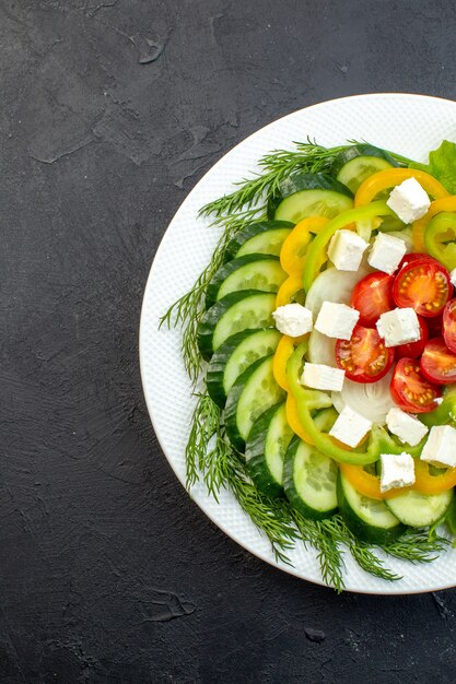 vista superior salada de vegetais consiste em fatias de pepino, tomate pimenta e queijo em fundo escuro