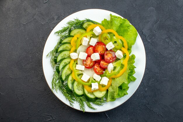 vista superior salada de vegetais consiste em fatias de pepino, tomate pimenta e queijo em fundo escuro