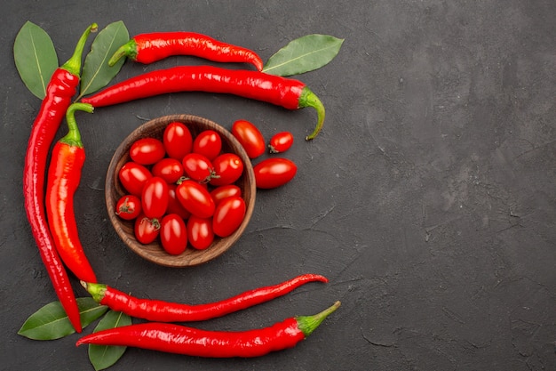 Vista superior semicírculo de pimentas vermelhas e folhas de louro e uma tigela de tomates cereja no lado esquerdo da mesa preta