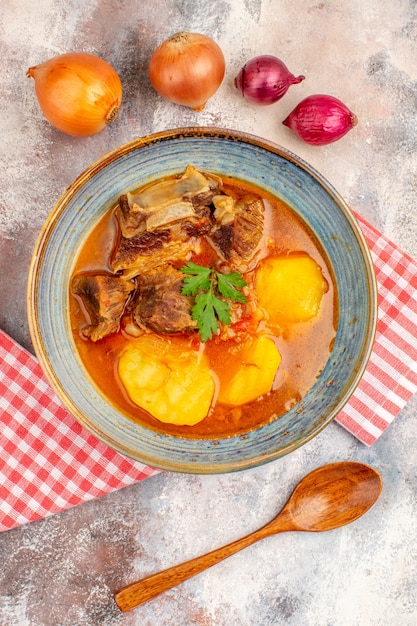 Vista superior sopa bozbash com colher de pau cebola amarela e vermelha em fundo nude