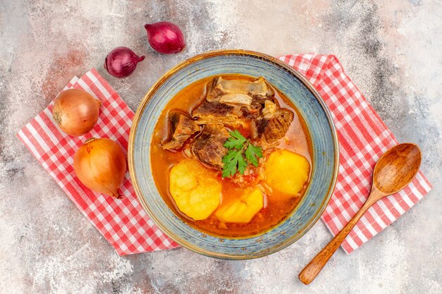 Vista superior sopa bozbash toalha de cozinha uma colher de pau cebola amarela e vermelha em fundo nude