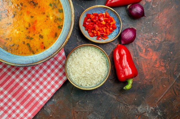 Vista superior sopa de arroz em uma tigela na toalha de mesa quadriculada branca vermelha pimentões cebolas outros alimentos em tigelas no fundo