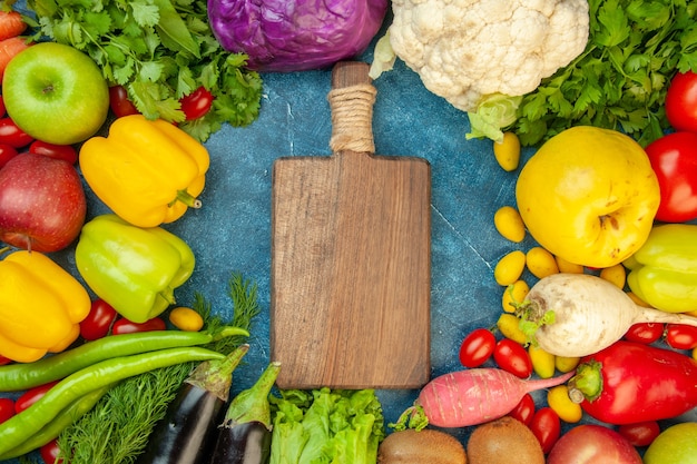 Vista superior Tábua de corte tomate cereja cumcuat marmelo maçãs beringelas rabanete coentro couve-flor couve-flor na mesa azul