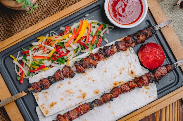 Vista superior tike kebab no espeto no pão pita com salada de legumes e ketchup