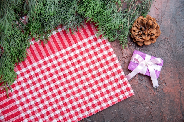 Foto grátis vista superior toalha de mesa quadriculada vermelha e branca pinetree ramos pinha presente de natal em fundo vermelho escuro