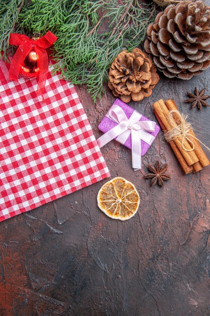 Vista superior toalha de mesa quadriculada vermelha e branca pinetree ramos pinhas presente de natal canela brinquedo bola de árvore de natal na superfície vermelho escuro