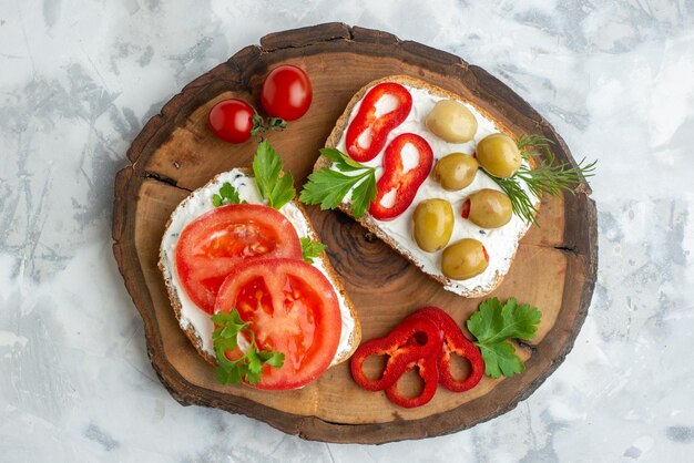 Vista superior torradas saborosas com tomates e azeitonas na placa de madeira fundo branco hambúrguer pão refeição horizontal comida jantar almoço sanduíche